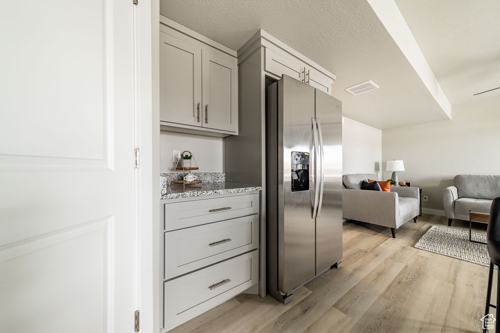 Kitchen with stainless steel fridge, gray cabinets, light wood-type flooring, open floor plan, and light stone countertops