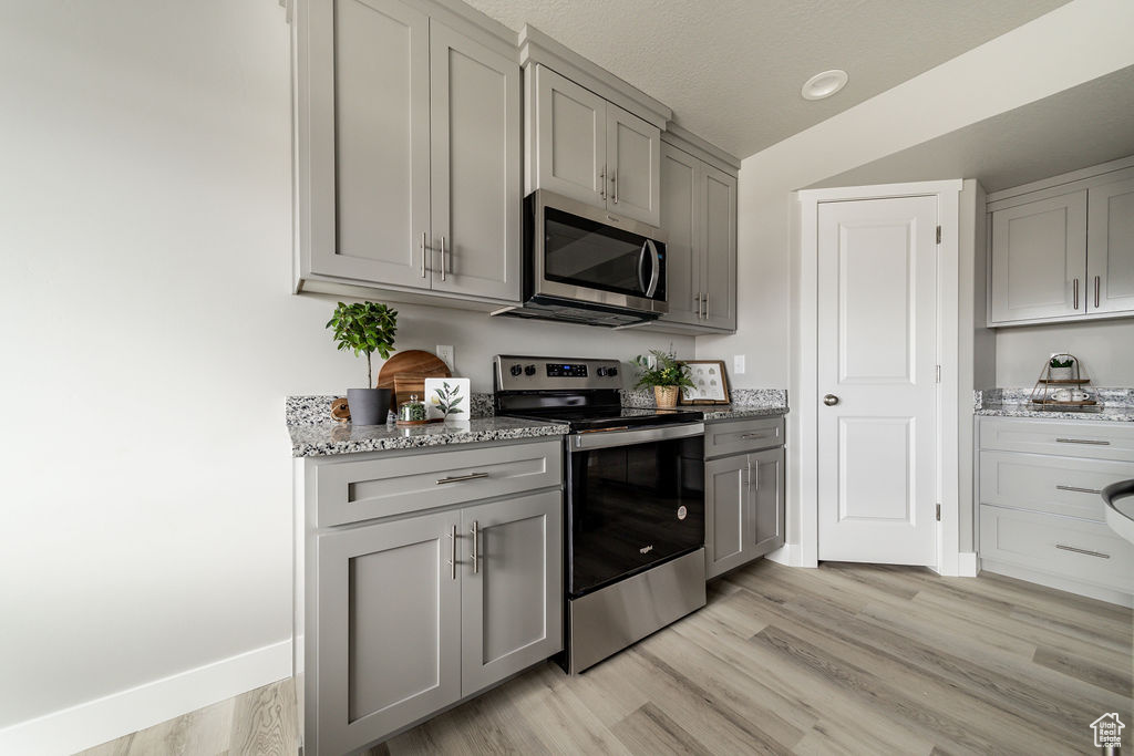 Kitchen with stainless steel appliances, gray cabinets, light stone countertops, and light wood-style floors