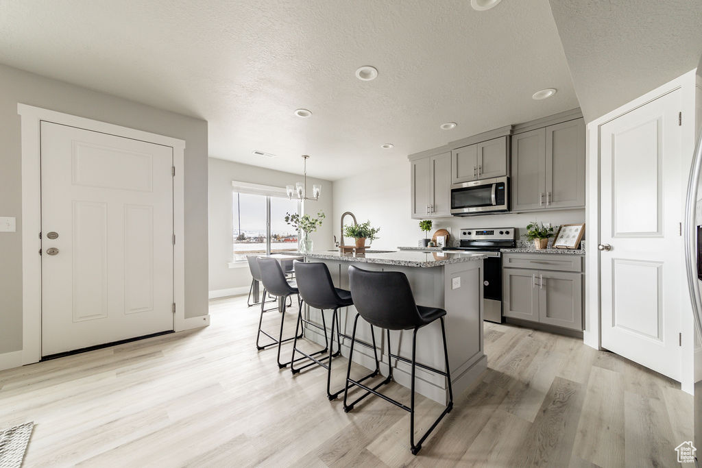 Kitchen featuring appliances with stainless steel finishes, gray cabinets, light stone countertops, a chandelier, and a kitchen bar