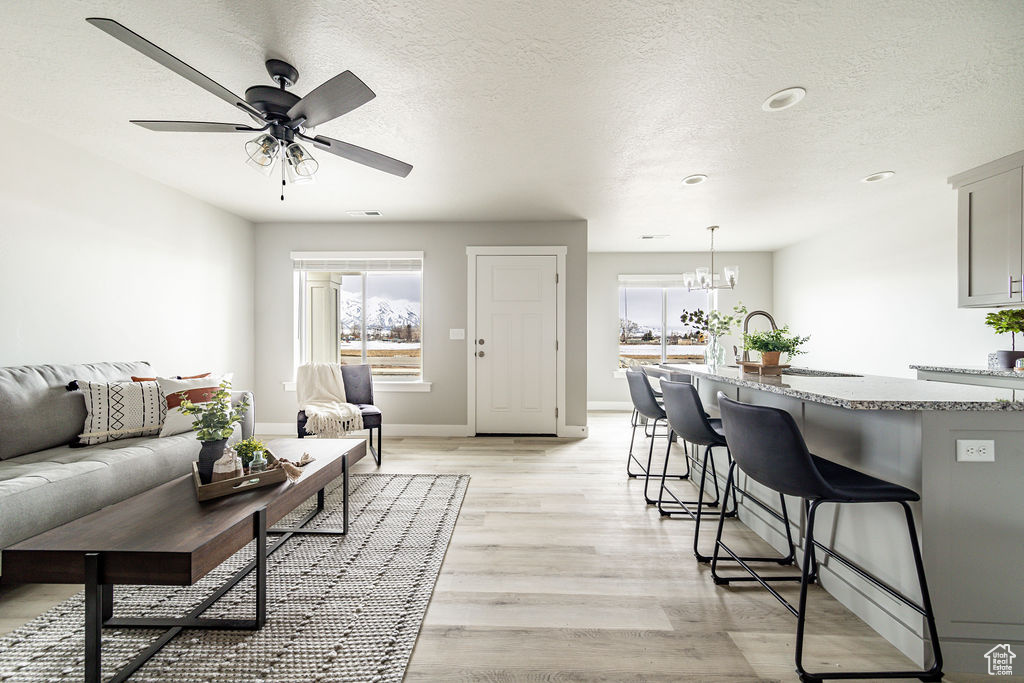 Living area featuring light wood-style floors, healthy amount of natural light, a textured ceiling, a ceiling fan, and a chandelier