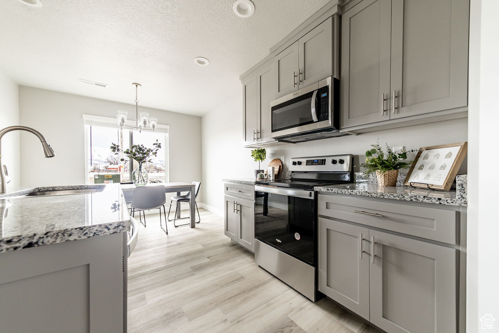 Kitchen with gray cabinets, appliances with stainless steel finishes, light wood finished floors, light stone countertops, and a textured ceiling