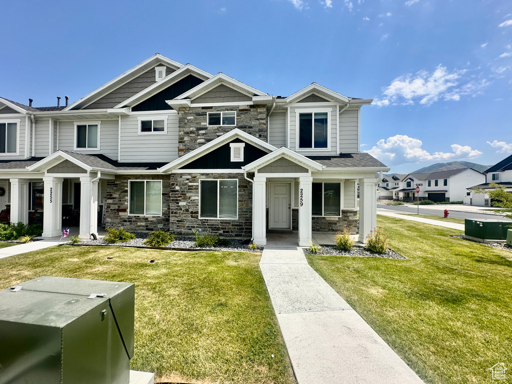 View of front of house featuring stone siding, a front yard, covered porch, and board and batten siding