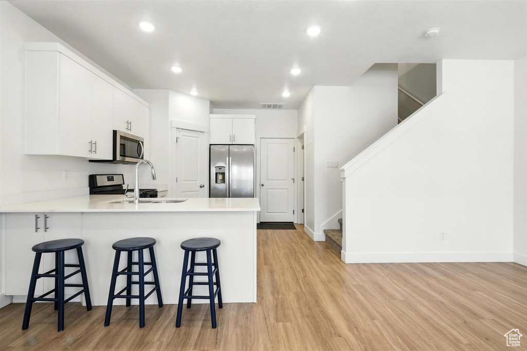 Kitchen featuring stainless steel appliances, light wood-type flooring, a peninsula, a kitchen bar, and recessed lighting