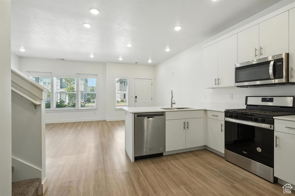 Kitchen with appliances with stainless steel finishes, light wood-style flooring, a peninsula, recessed lighting, and white cabinetry