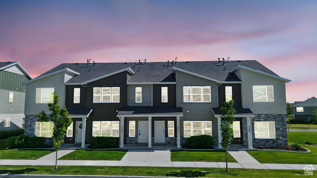 Townhome / multi-family property featuring a front yard, stone siding, and roof with shingles