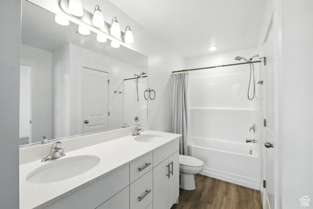 Full bath featuring shower / bath combo, double vanity, and wood finished floors
