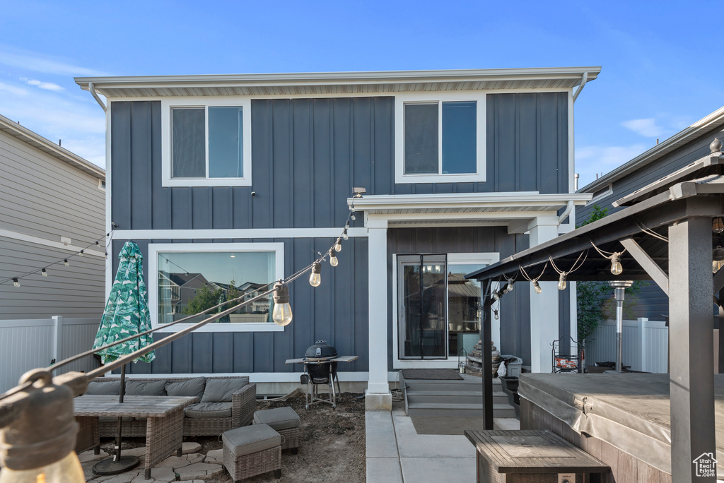Back of house with board and batten siding, a patio area, an outdoor living space, and a gazebo