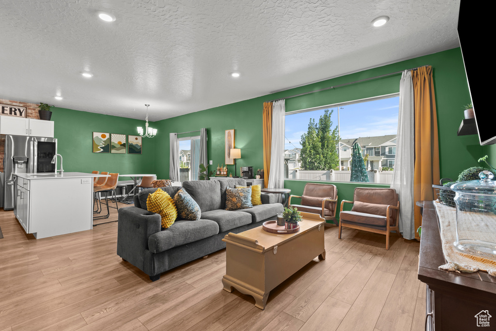 Living room with a chandelier, light wood-type flooring, a textured ceiling, and recessed lighting