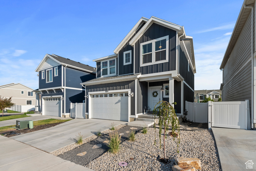 View of front of house with board and batten siding, an attached garage, driveway, and a gate