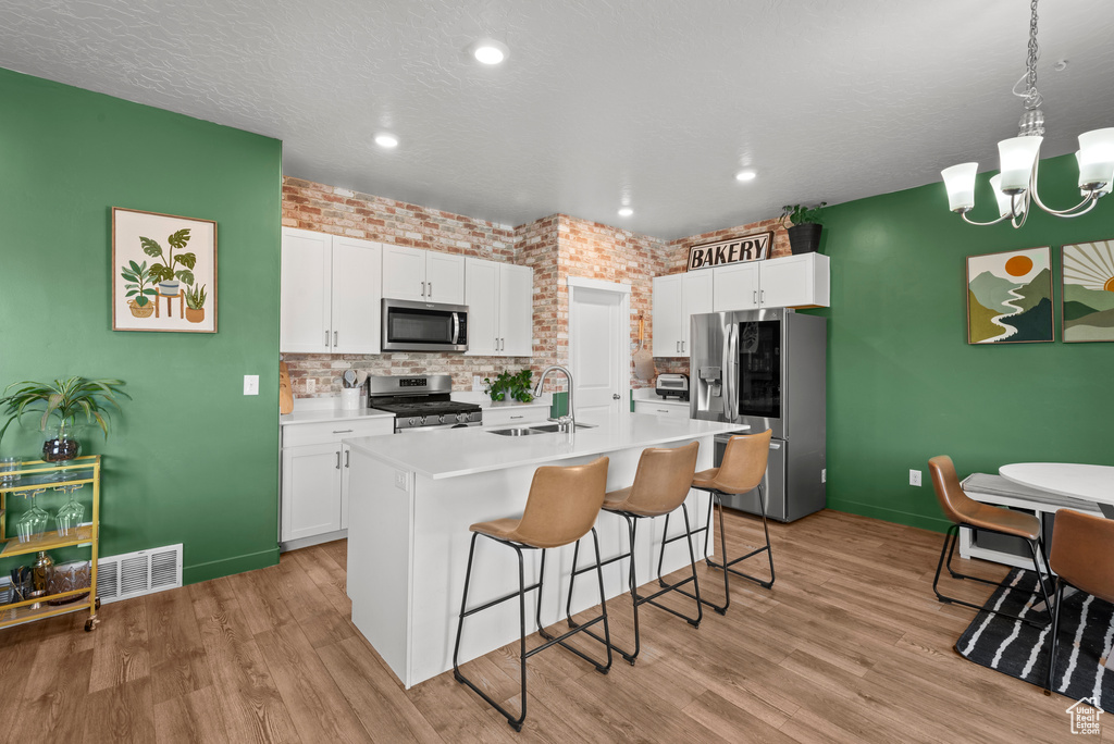 Kitchen with stainless steel appliances, a kitchen breakfast bar, a kitchen island with sink, white cabinetry, and recessed lighting