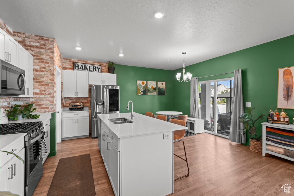 Kitchen with appliances with stainless steel finishes, a breakfast bar, a chandelier, white cabinetry, and light wood-type flooring