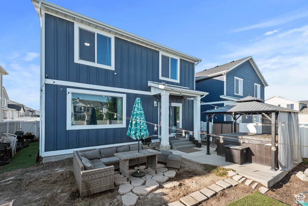 Back of property featuring a hot tub, a gazebo, a patio area, and board and batten siding