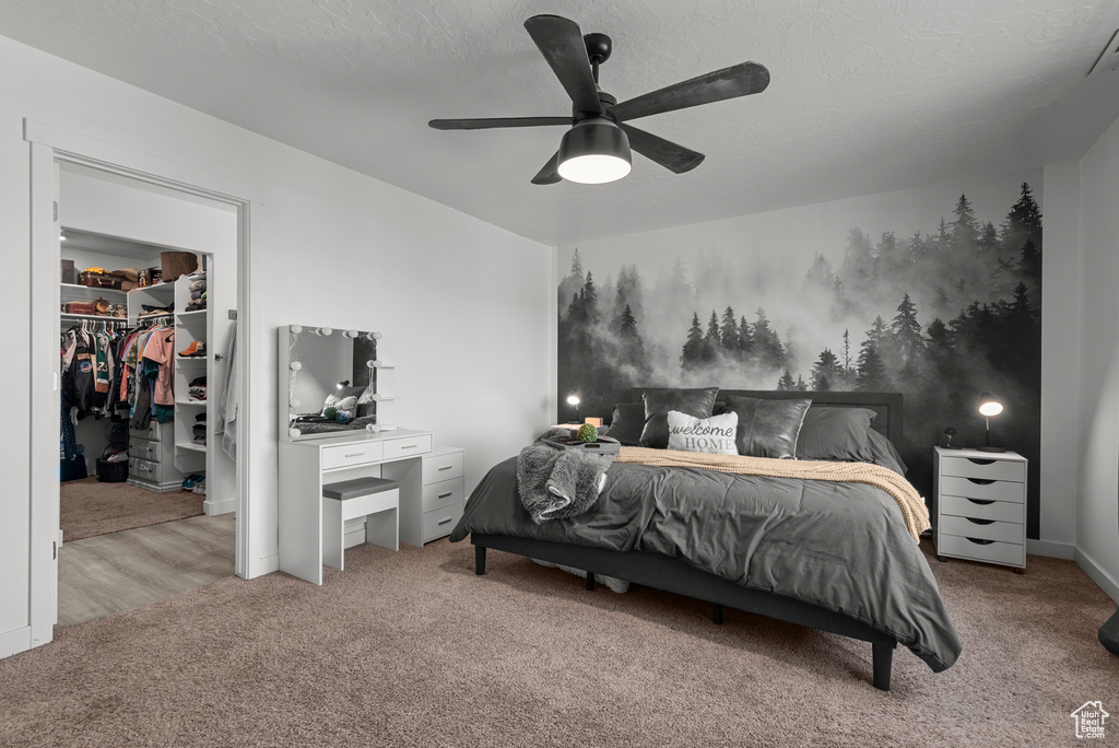 Bedroom featuring carpet, a walk in closet, a closet, a ceiling fan, and a textured ceiling