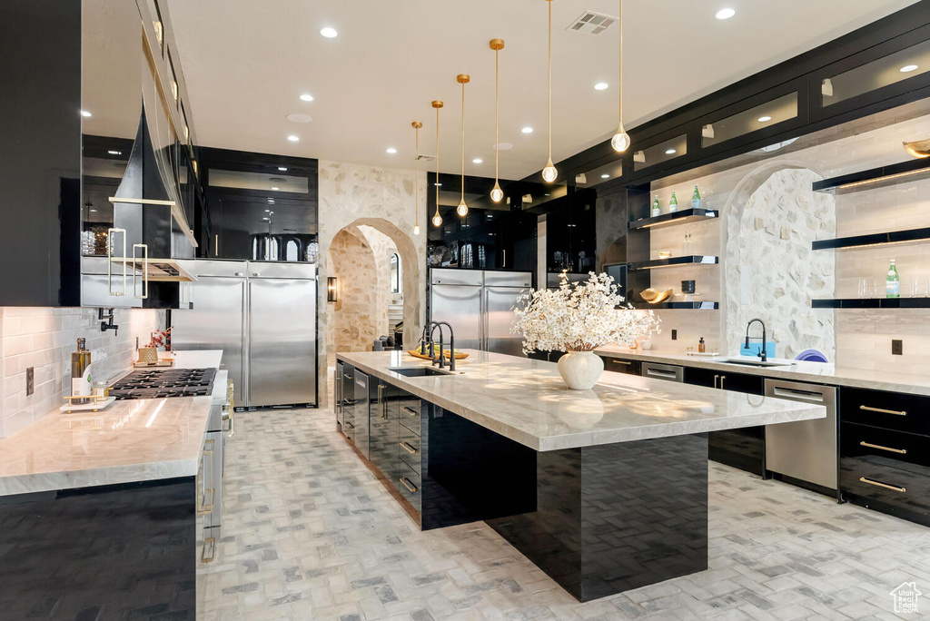 Kitchen with dark cabinetry, stainless steel appliances, decorative backsplash, open shelves, and pendant lighting