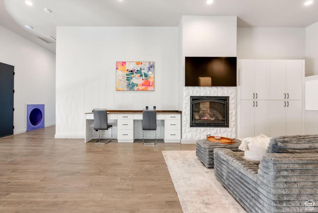 Living room with light wood finished floors, built in desk, recessed lighting, and a glass covered fireplace