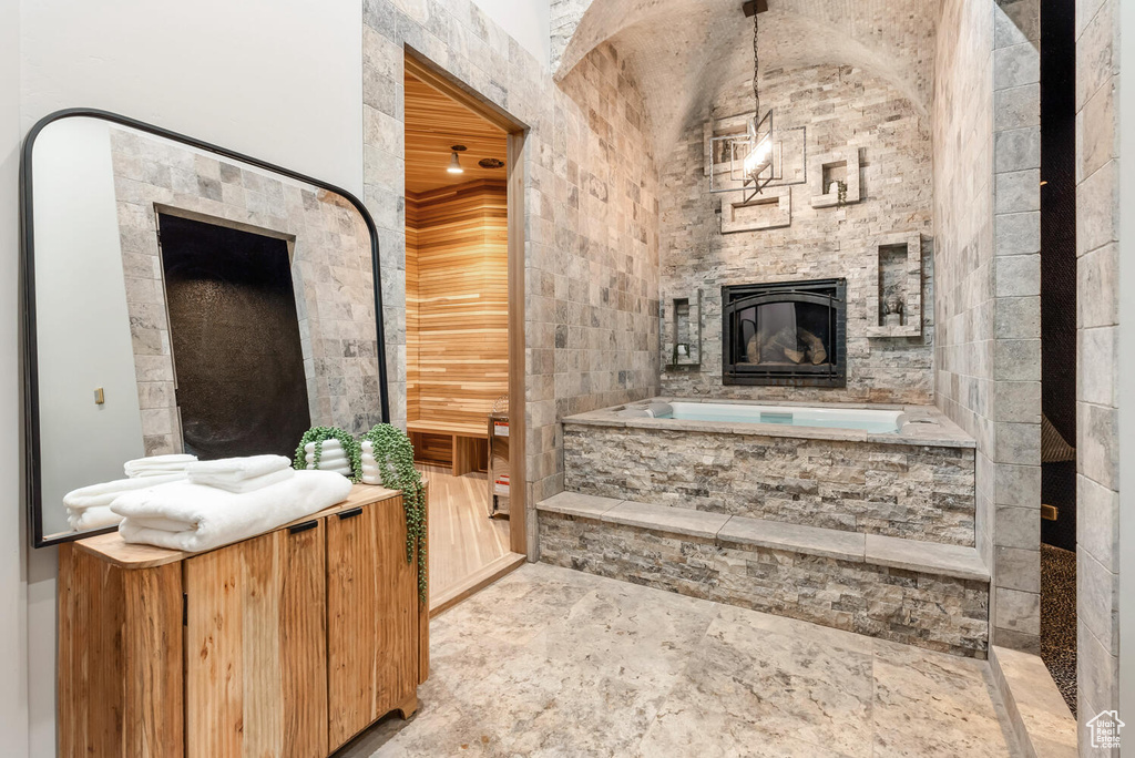 Bathroom with a stone fireplace, a bath, and vaulted ceiling
