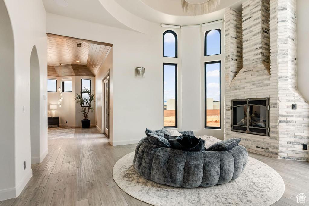 Living area featuring a fireplace, arched walkways, light wood-type flooring, vaulted ceiling, and wooden ceiling