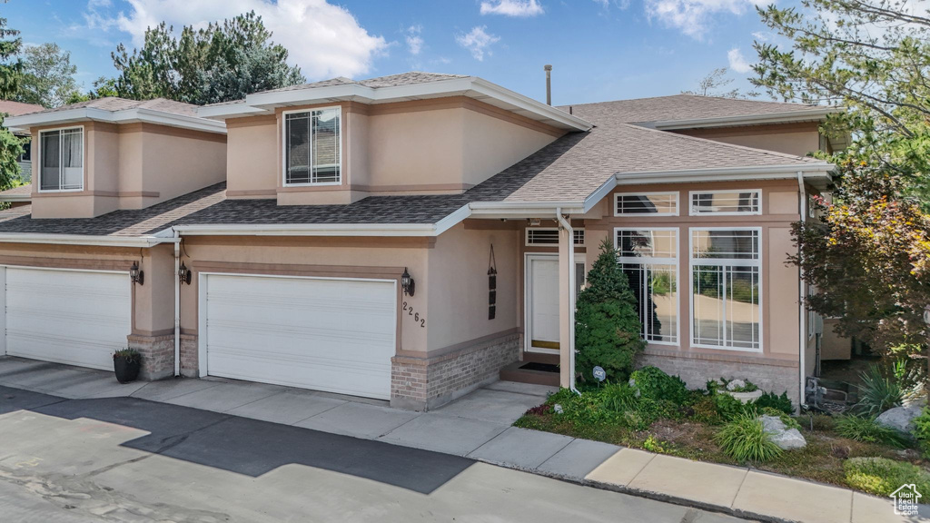 View of front of property with an attached garage, stucco siding, brick siding, a shingled roof, and driveway