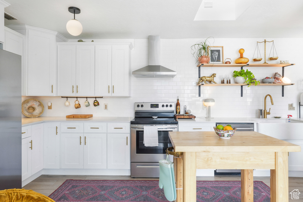 Kitchen with appliances with stainless steel finishes, wall chimney exhaust hood, white cabinets, and light wood finished floors