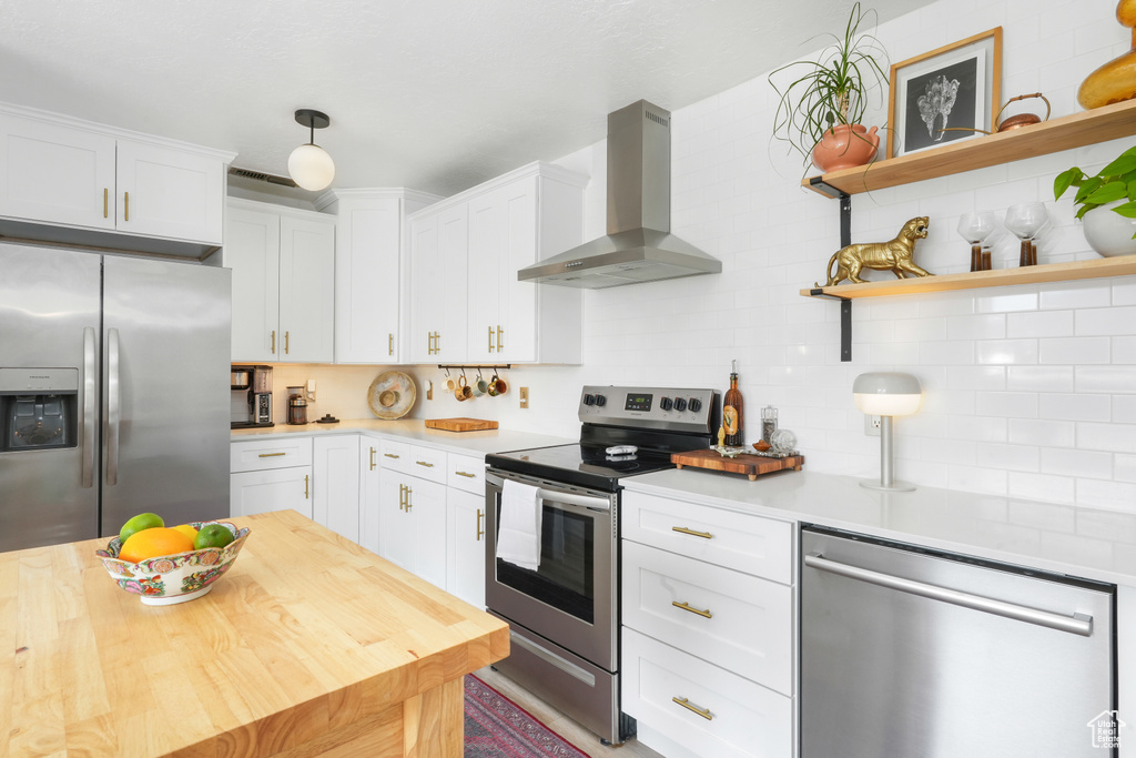 Kitchen with wall chimney exhaust hood, stainless steel appliances, white cabinets, and tasteful backsplash
