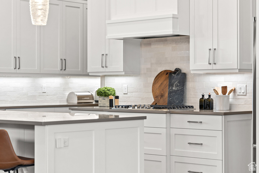 Kitchen featuring backsplash, custom range hood, stainless steel gas cooktop, and white cabinetry