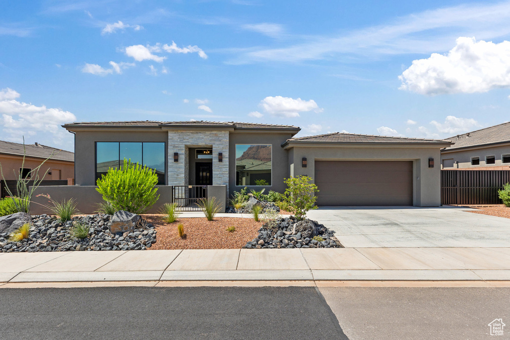 View of front of property with a garage, stucco siding, driveway, stone siding, and a tile roof