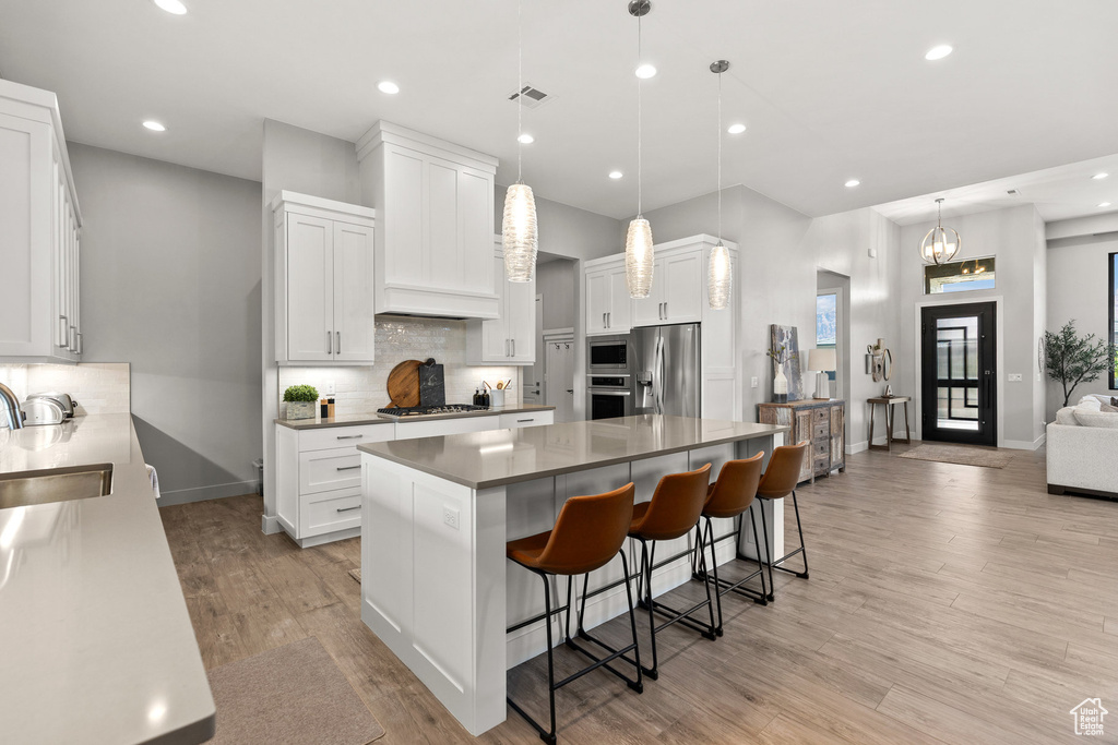 Kitchen featuring stainless steel appliances, a center island, decorative backsplash, a breakfast bar area, and light wood-type flooring