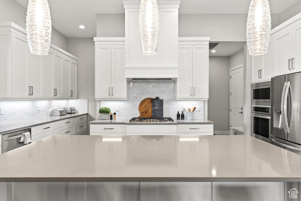 Kitchen featuring stainless steel appliances, decorative backsplash, white cabinetry, and recessed lighting