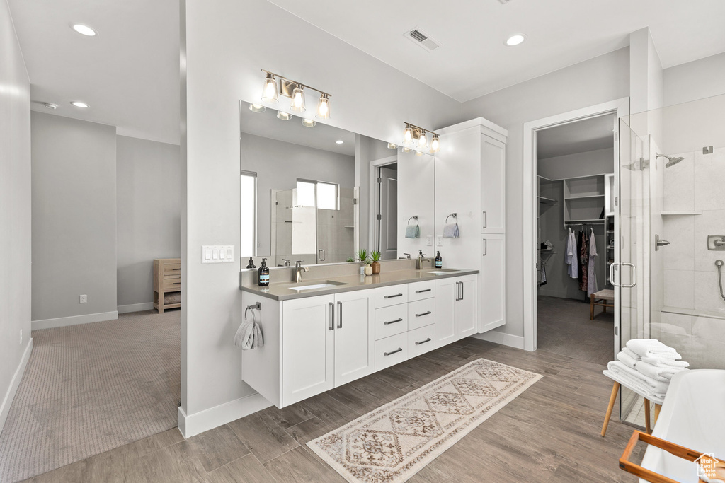 Full bathroom with double vanity, a shower stall, a spacious closet, wood finished floors, and recessed lighting