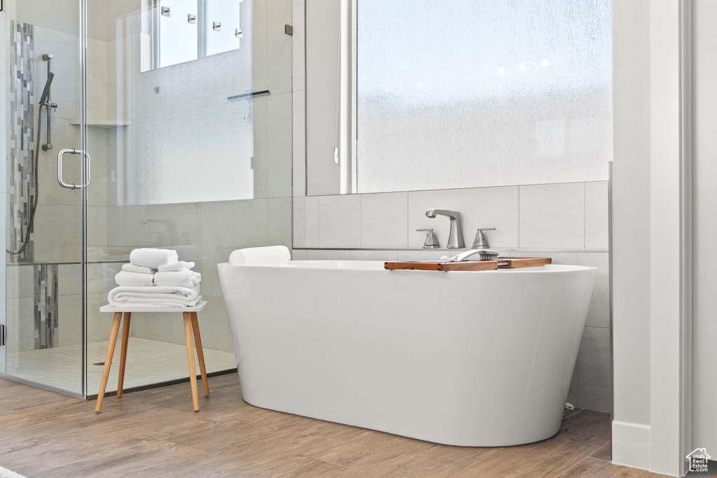 Bathroom with tile walls, wood finished floors, a shower with shower door, and a freestanding bath
