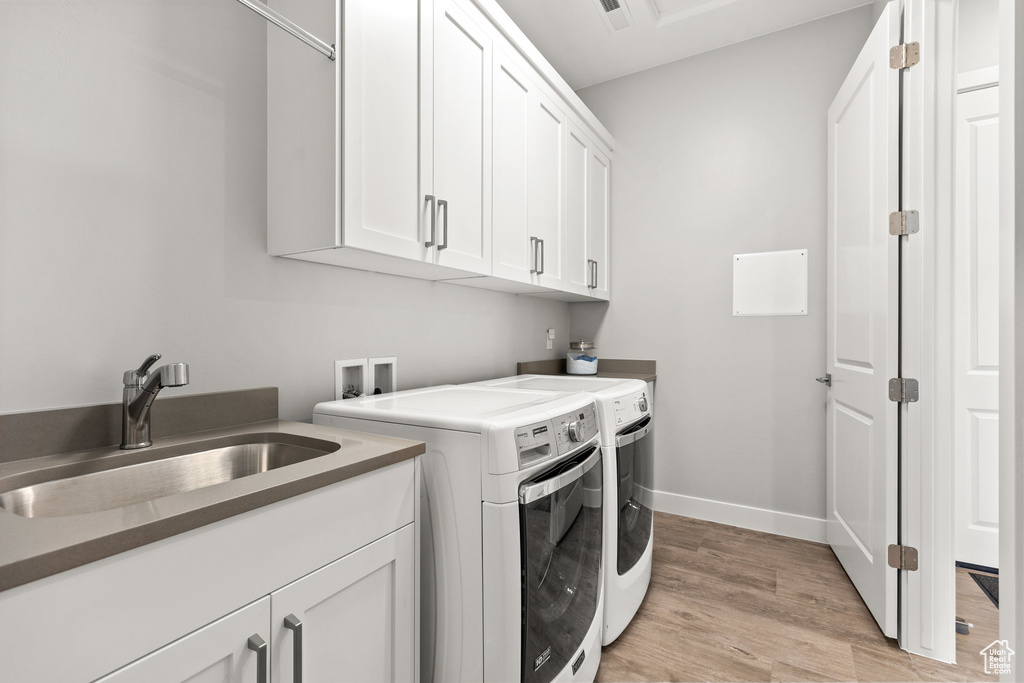 Laundry room with washing machine and clothes dryer, cabinet space, and light wood-style floors