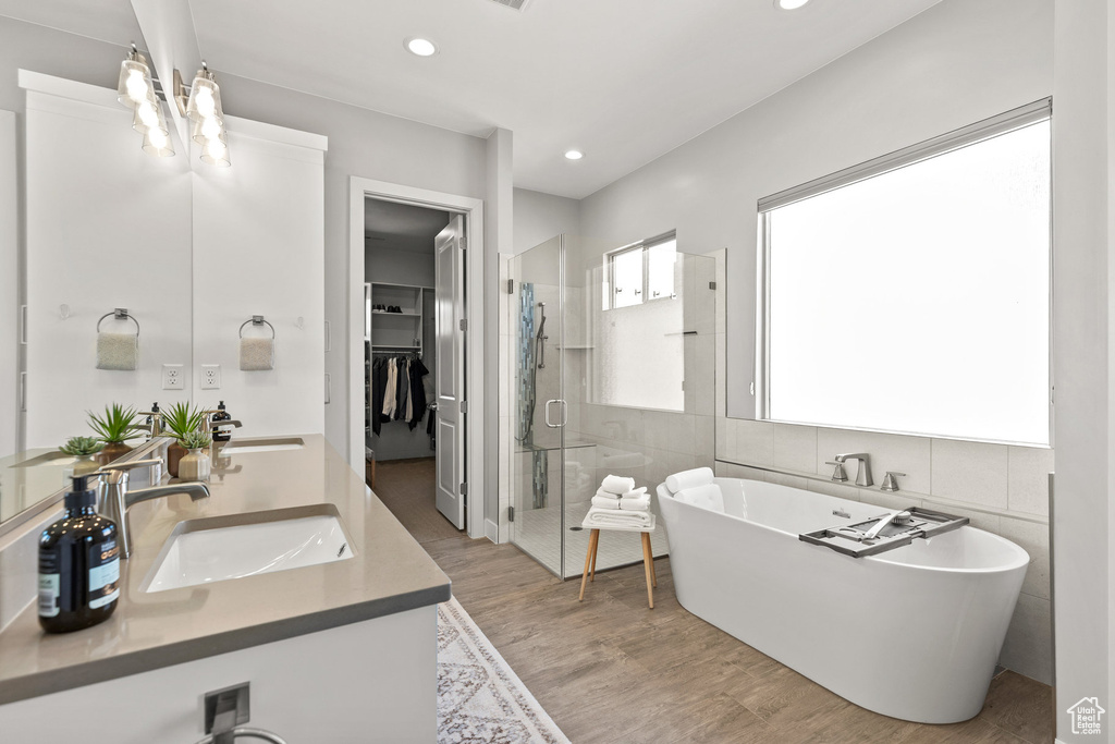 Full bath featuring a shower stall, double vanity, a soaking tub, wood finished floors, and recessed lighting