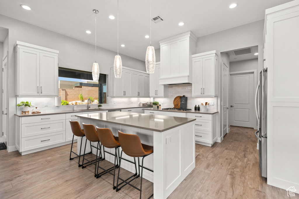 Kitchen with a center island, stainless steel appliances, white cabinets, a kitchen bar, and tasteful backsplash