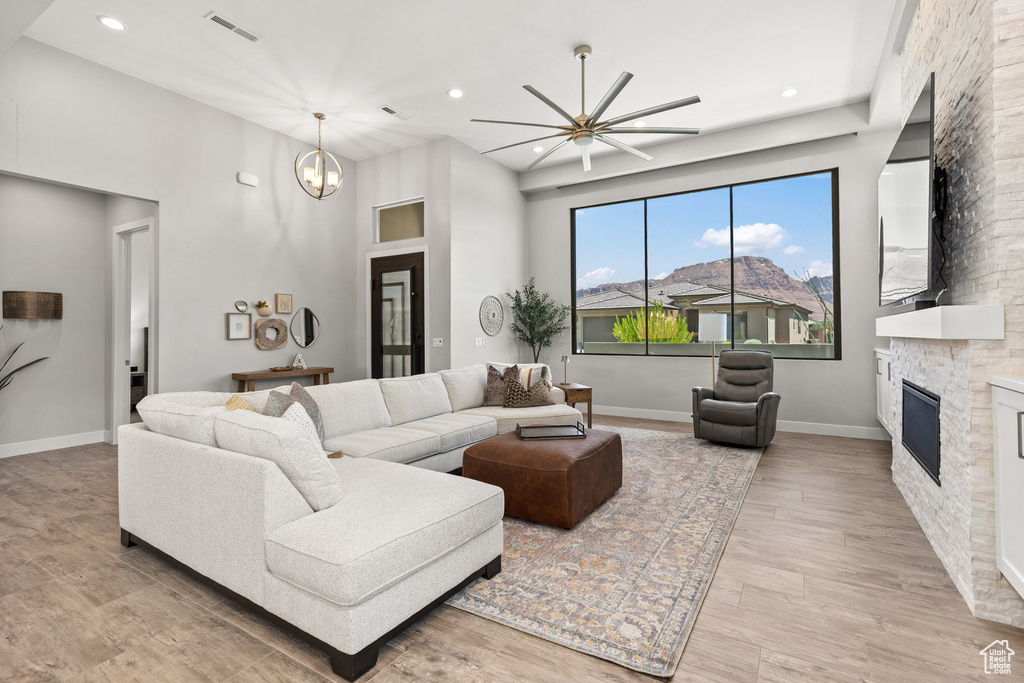Living room featuring a stone fireplace, light wood-style flooring, recessed lighting, a chandelier, and a ceiling fan