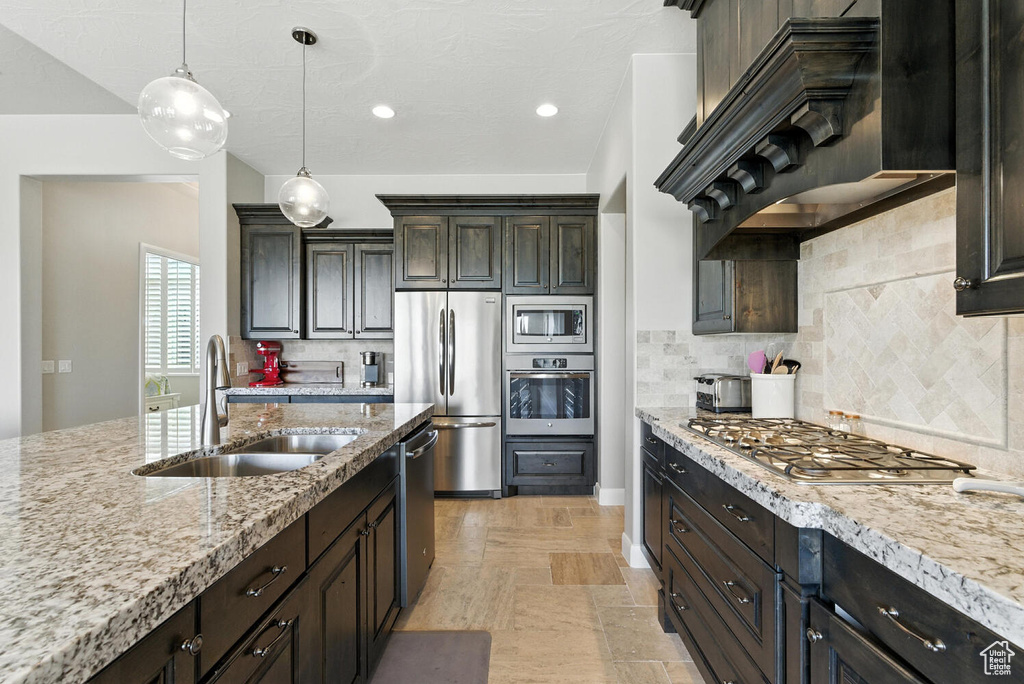 Kitchen featuring stainless steel appliances, decorative backsplash, decorative light fixtures, light stone countertops, and premium range hood