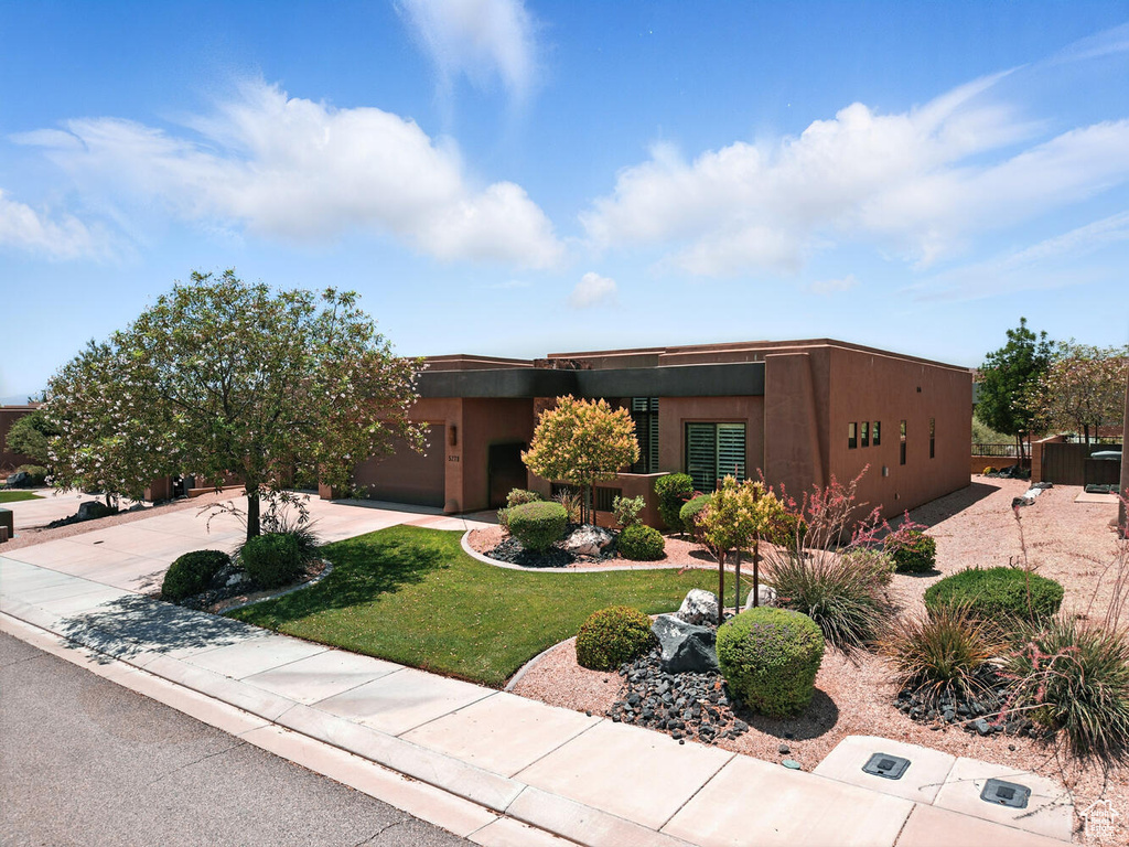 Pueblo revival-style home with driveway, a garage, a front yard, and stucco siding