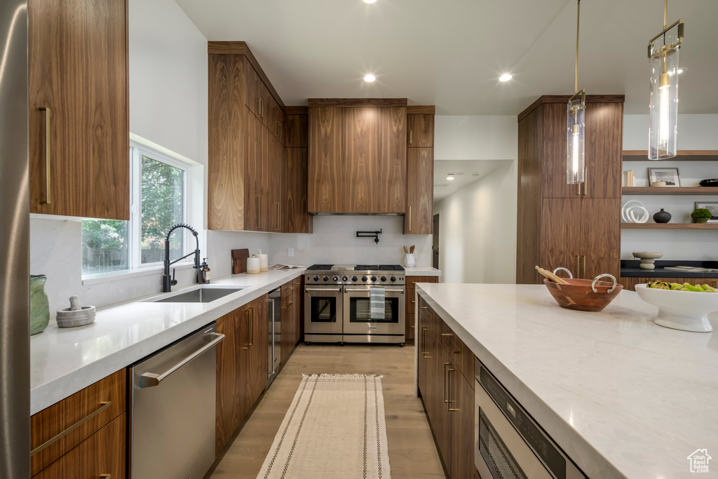 Kitchen with appliances with stainless steel finishes, modern cabinets, light wood finished floors, hanging light fixtures, and brown cabinets