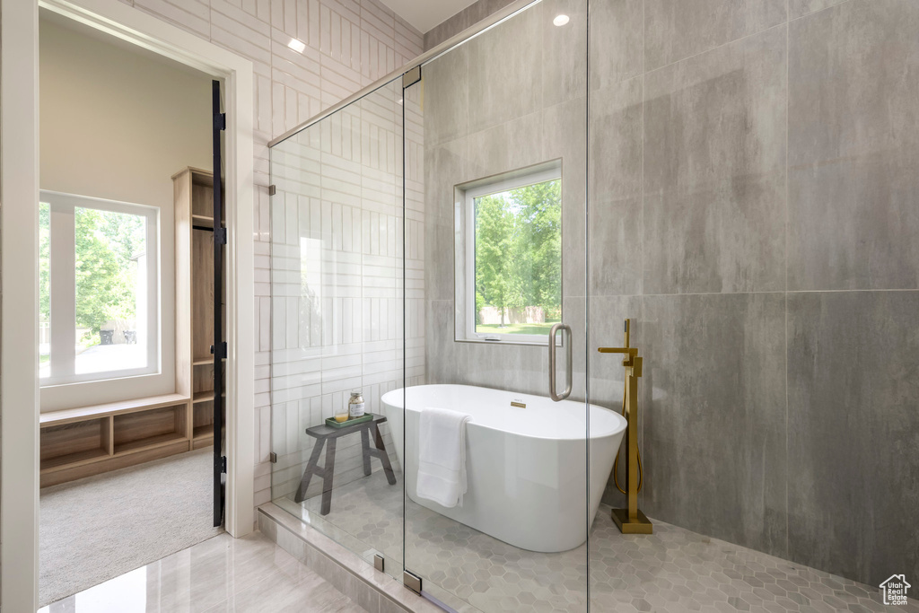 Bathroom featuring healthy amount of natural light, a stall shower, a soaking tub, tile walls, and tile patterned flooring