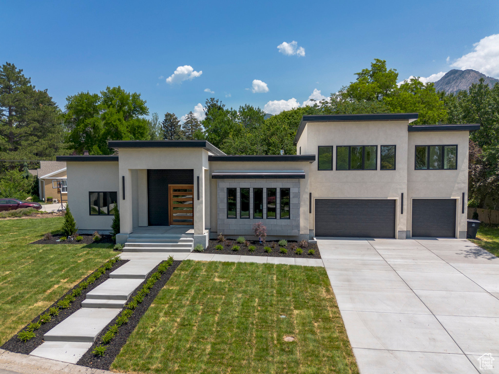 Contemporary house featuring a garage, stucco siding, concrete driveway, a front lawn, and a mountain view