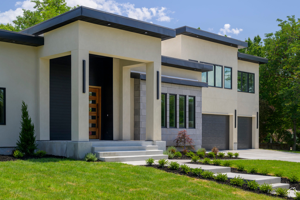 Contemporary house featuring stucco siding, concrete driveway, an attached garage, and a front lawn