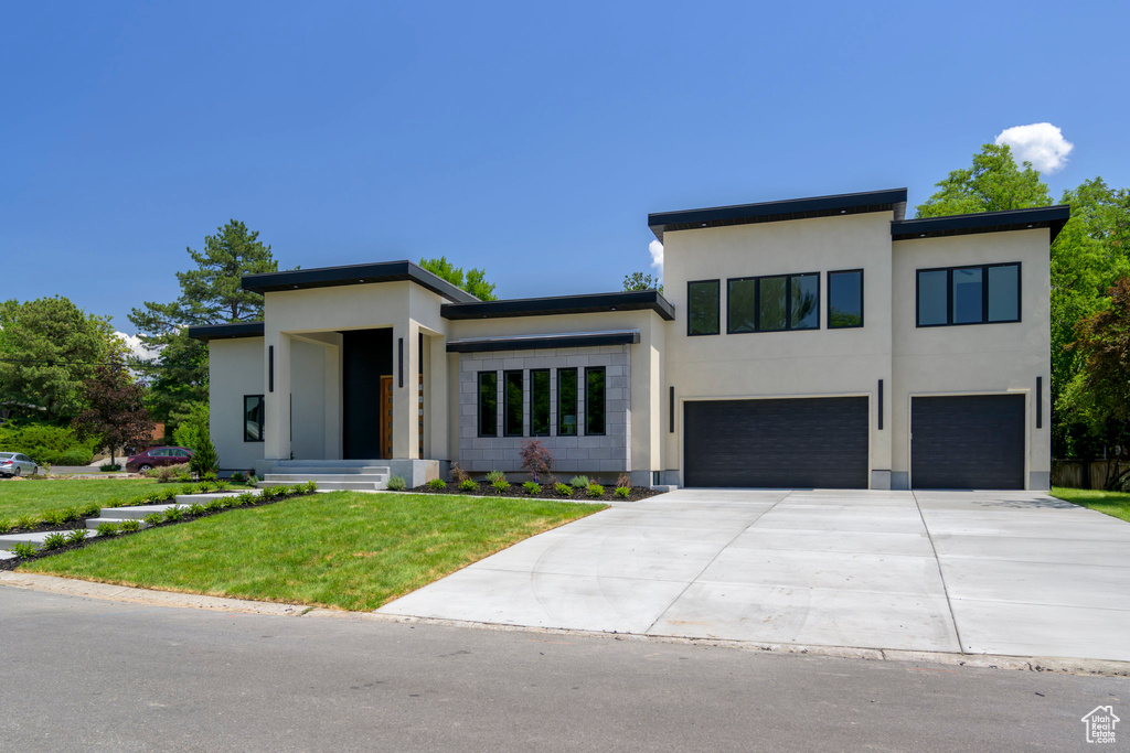 Contemporary home featuring an attached garage, driveway, a front yard, and stucco siding
