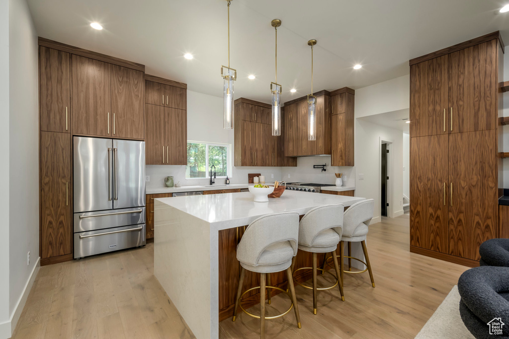 Kitchen featuring high quality fridge, light wood-style flooring, light countertops, a kitchen breakfast bar, and a center island