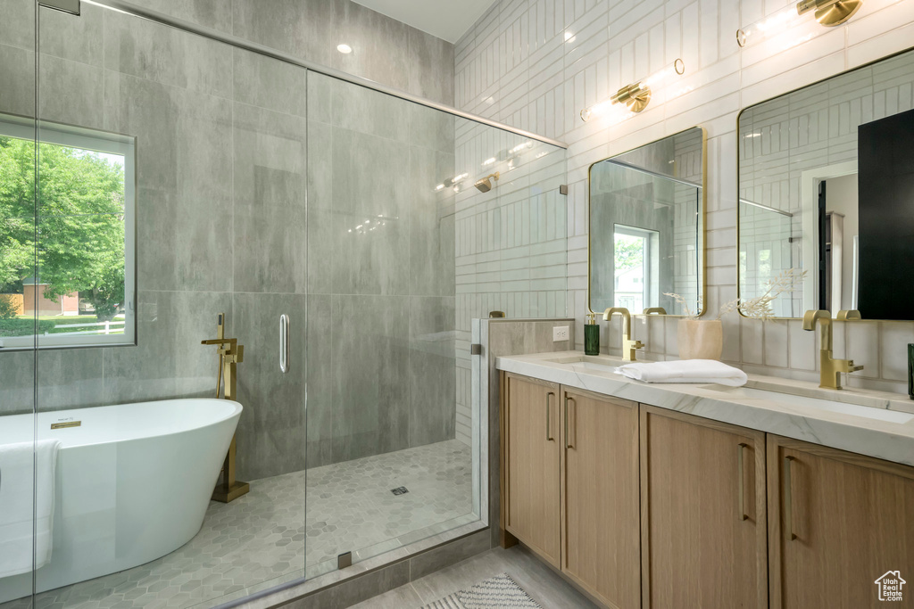 Bathroom with tile walls, a stall shower, a freestanding bath, double vanity, and healthy amount of natural light
