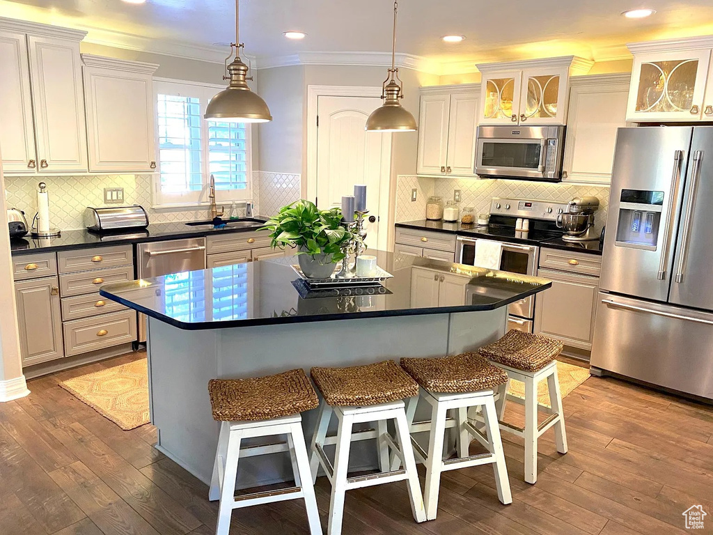Kitchen featuring appliances with stainless steel finishes, dark countertops, a kitchen breakfast bar, ornamental molding, and a kitchen island