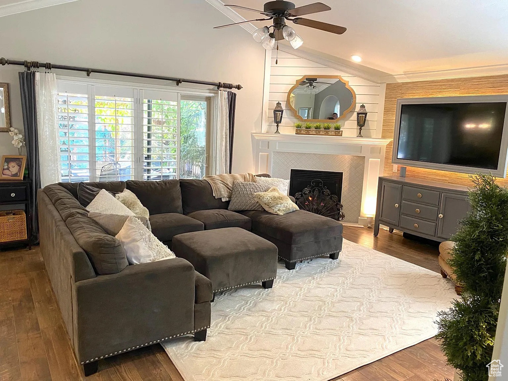 Living room featuring lofted ceiling, ceiling fan, wood finished floors, a tiled fireplace, and crown molding
