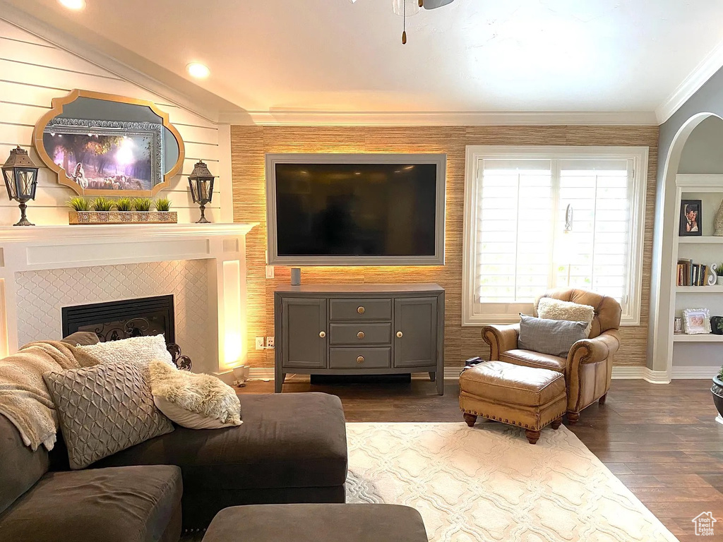 Living area featuring dark wood-style flooring, a tile fireplace, crown molding, and ceiling fan