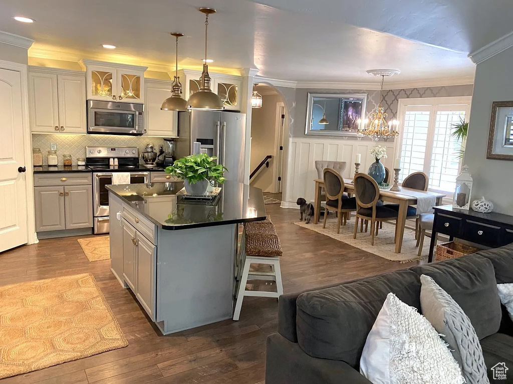 Kitchen featuring appliances with stainless steel finishes, crown molding, a chandelier, dark countertops, and arched walkways