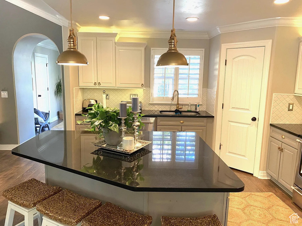 Kitchen featuring dark countertops, arched walkways, light wood-style flooring, ornamental molding, and decorative backsplash