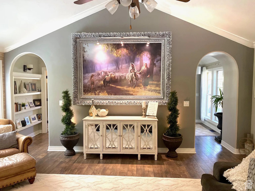 Living room featuring ceiling fan, vaulted ceiling, arched walkways, wood finished floors, and ornamental molding