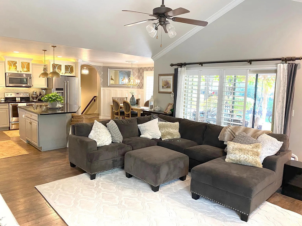 Living room featuring light wood-style flooring, a ceiling fan, a chandelier, ornamental molding, and high vaulted ceiling